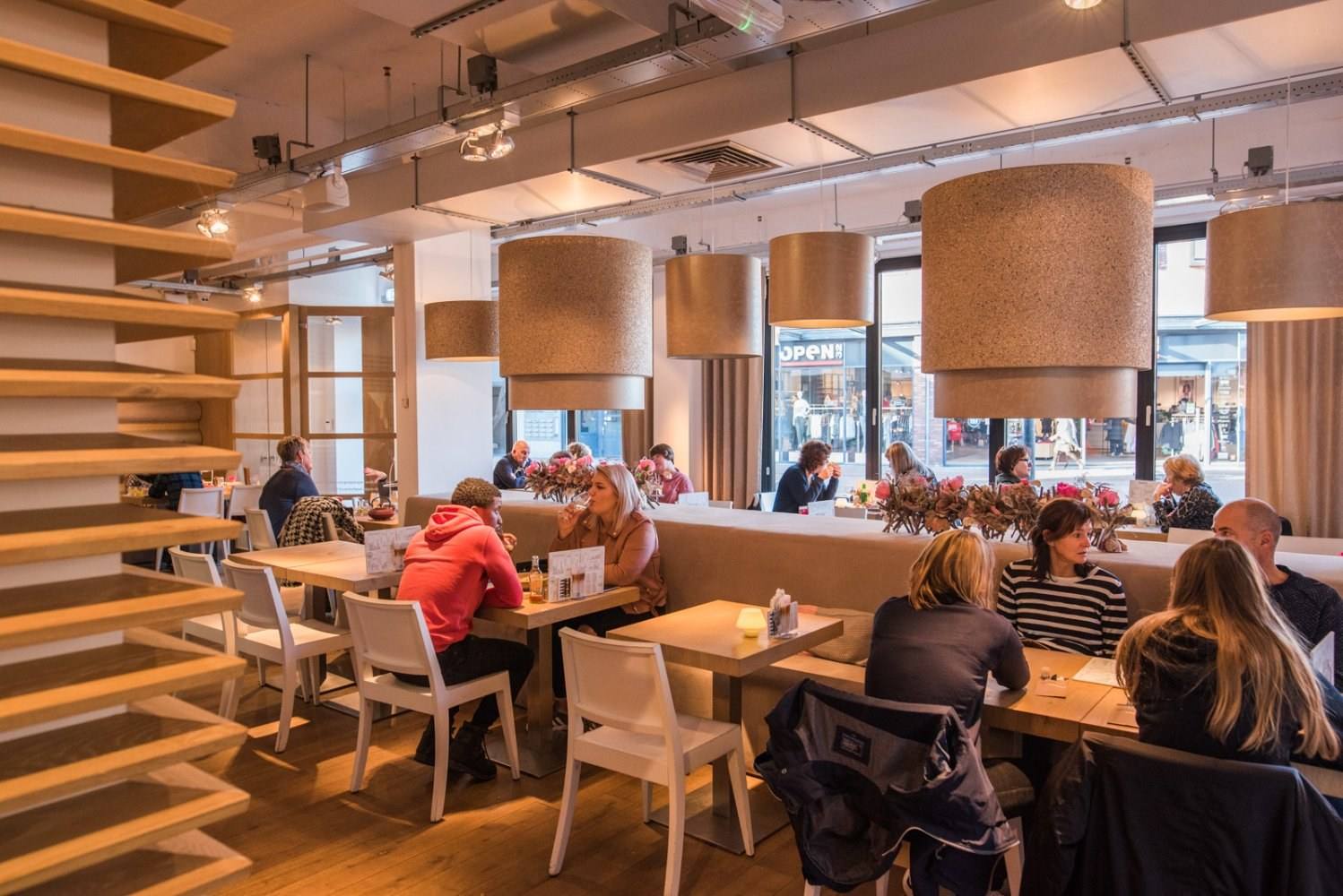 De eetzaal van Donker & Blond met houten tafels, witte stoelen en grote hanglampen